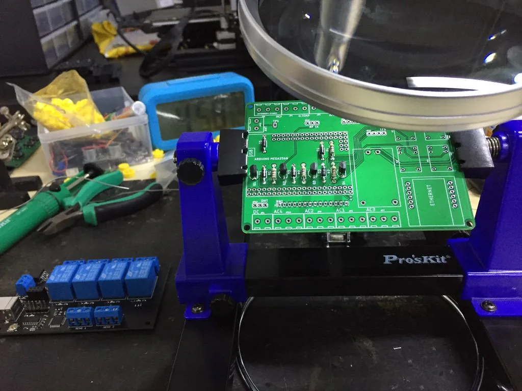 Arduino Mega 2560 baseboard during assembly in a PCB fixture, with a separate relay board on the workbench